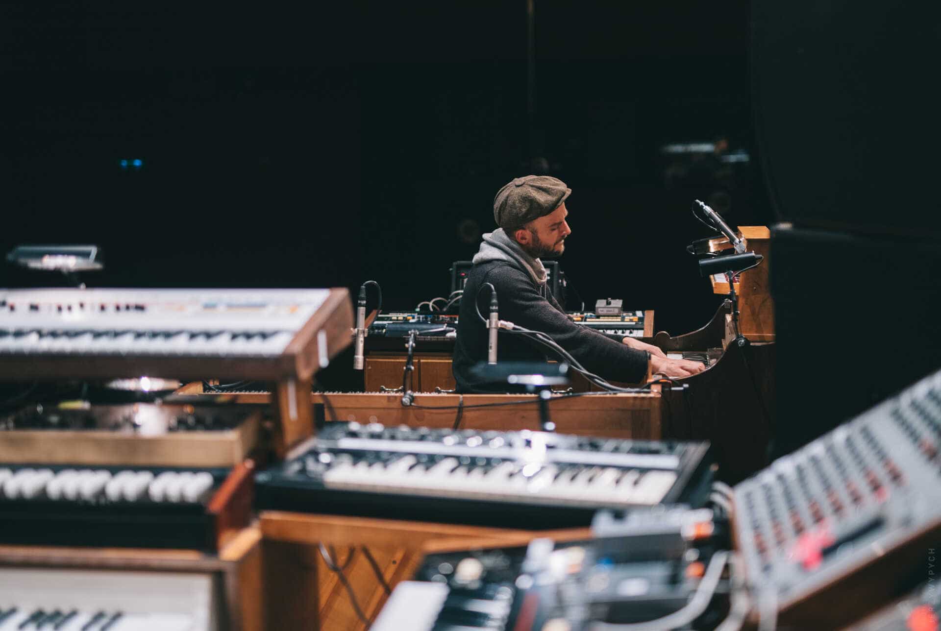 Nils Frahm playing a piano, surrounded by musical instruments.